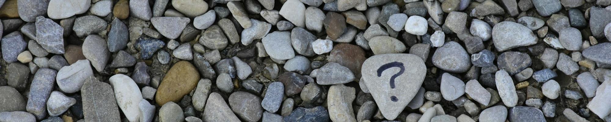 A photo with many small stones, one having a question mark on it